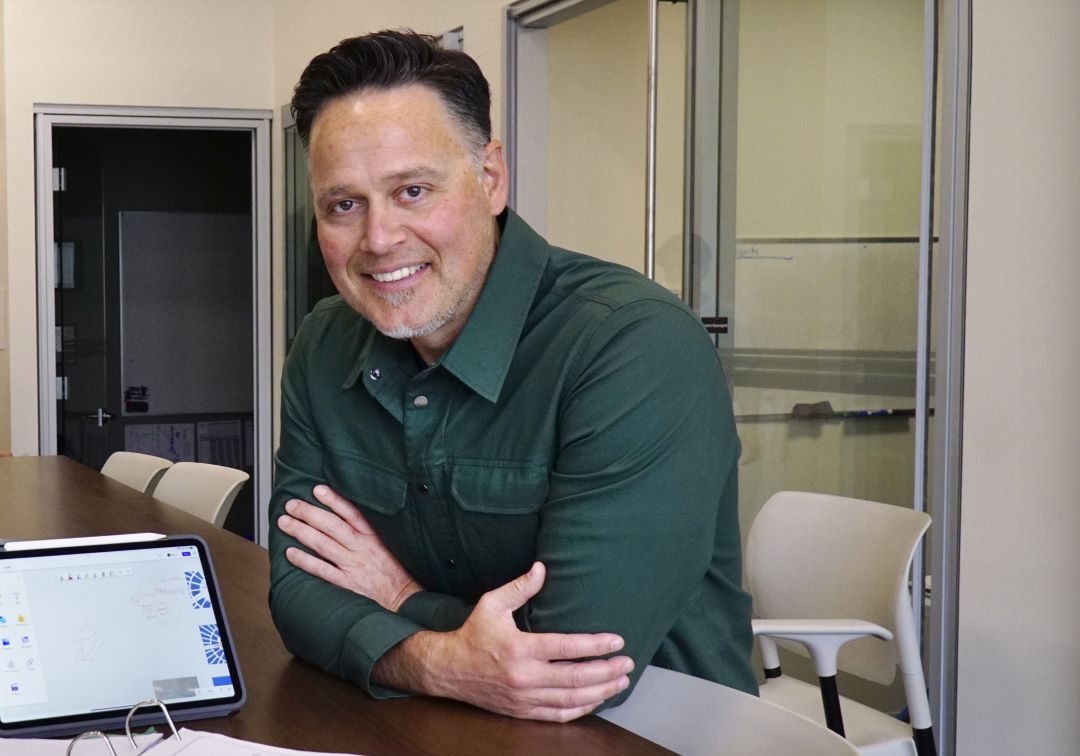 A smiling man leaning on a cabinet in his office building.