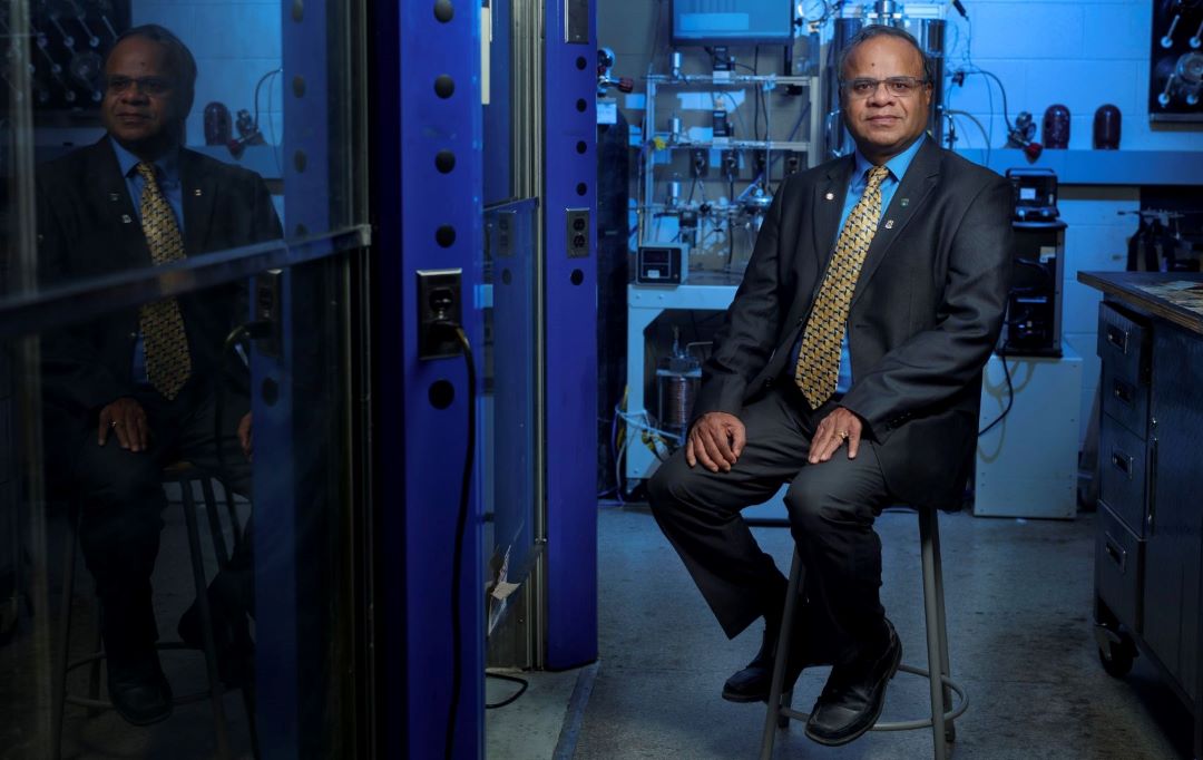 Male professor sits on a stool in a chemical engineering lab